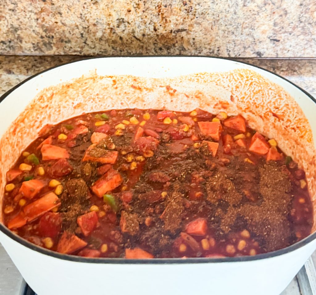 Tomatoes, sweet potatoes, corn, and kidney beans added to turkey chili in a Dutch oven